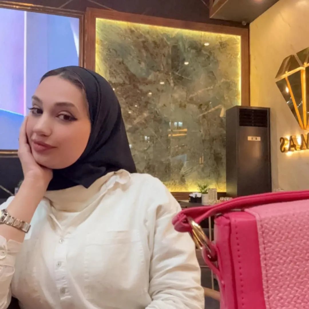 Image of 𝓜𝓪𝓻𝓲𝓪𝓶 𝓪𝓵 💕 from Instagram black hijab, white shirt, silver watch, pink handbag, indoor setting