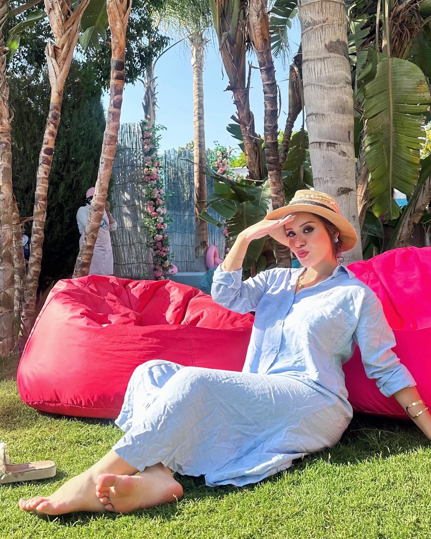 Image of • Salma yehia from Instagram light blue dress, straw hat, barefoot, outdoors, red bean bag, tropical plants