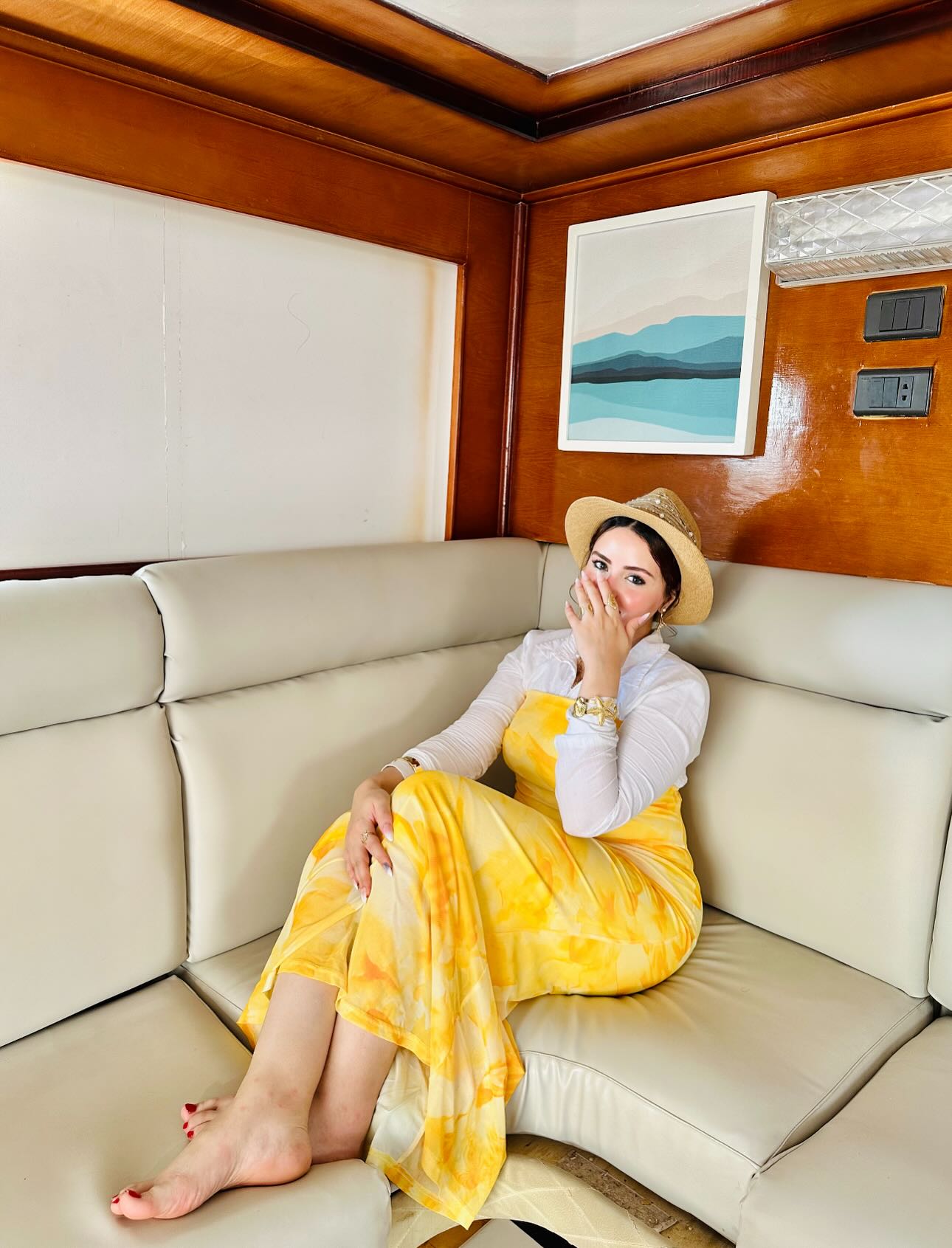 Image of AYA Elboghdady from Instagram yellow dress, white top, straw hat, bracelet, barefoot, indoor, couch, artwork