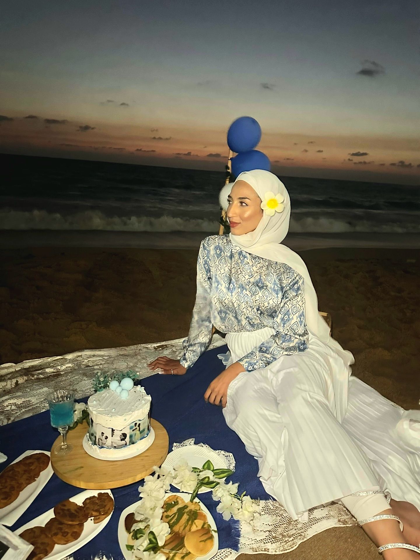 Image of Nour Abd Elrahman from Instagram blue patterned blouse, white pleated skirt, white hijab, flower accessory, silver sandals, beach, sunset, balloons, picnic