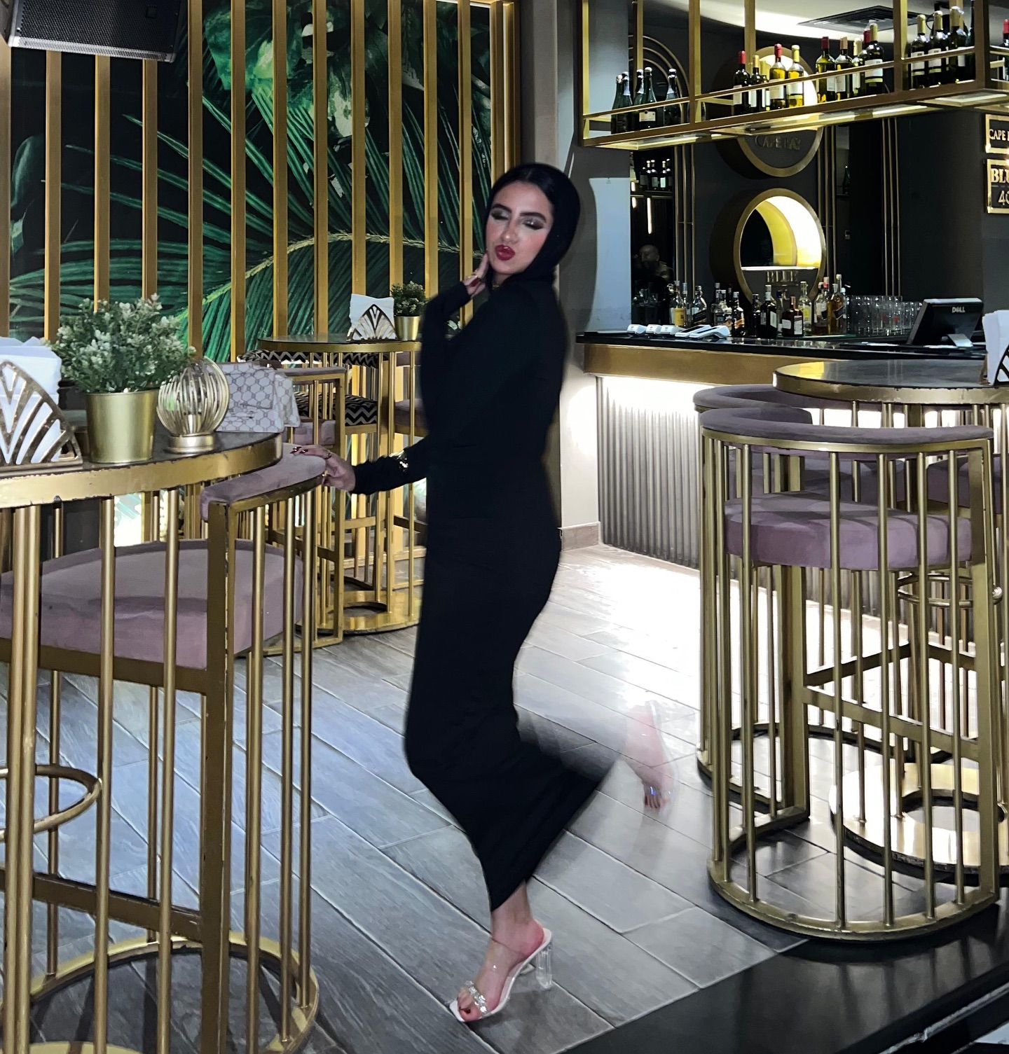 Image of Rawan Osman | روان عثمان from Instagram black dress, headscarf, transparent heels, bar, indoor