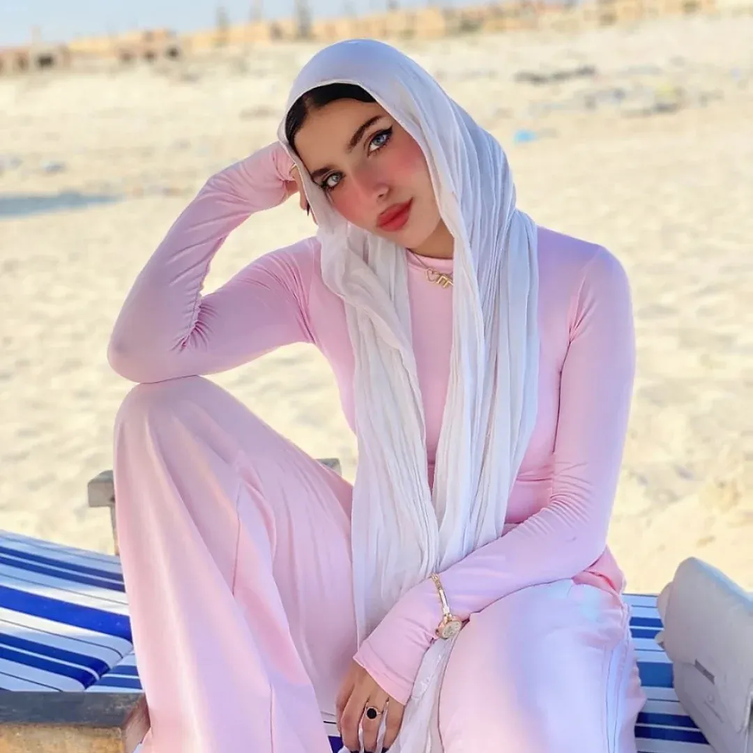 Image of Yasmin Samir from Instagram white hijab, pink outfit, bracelet, beach, blue striped towel, barefoot