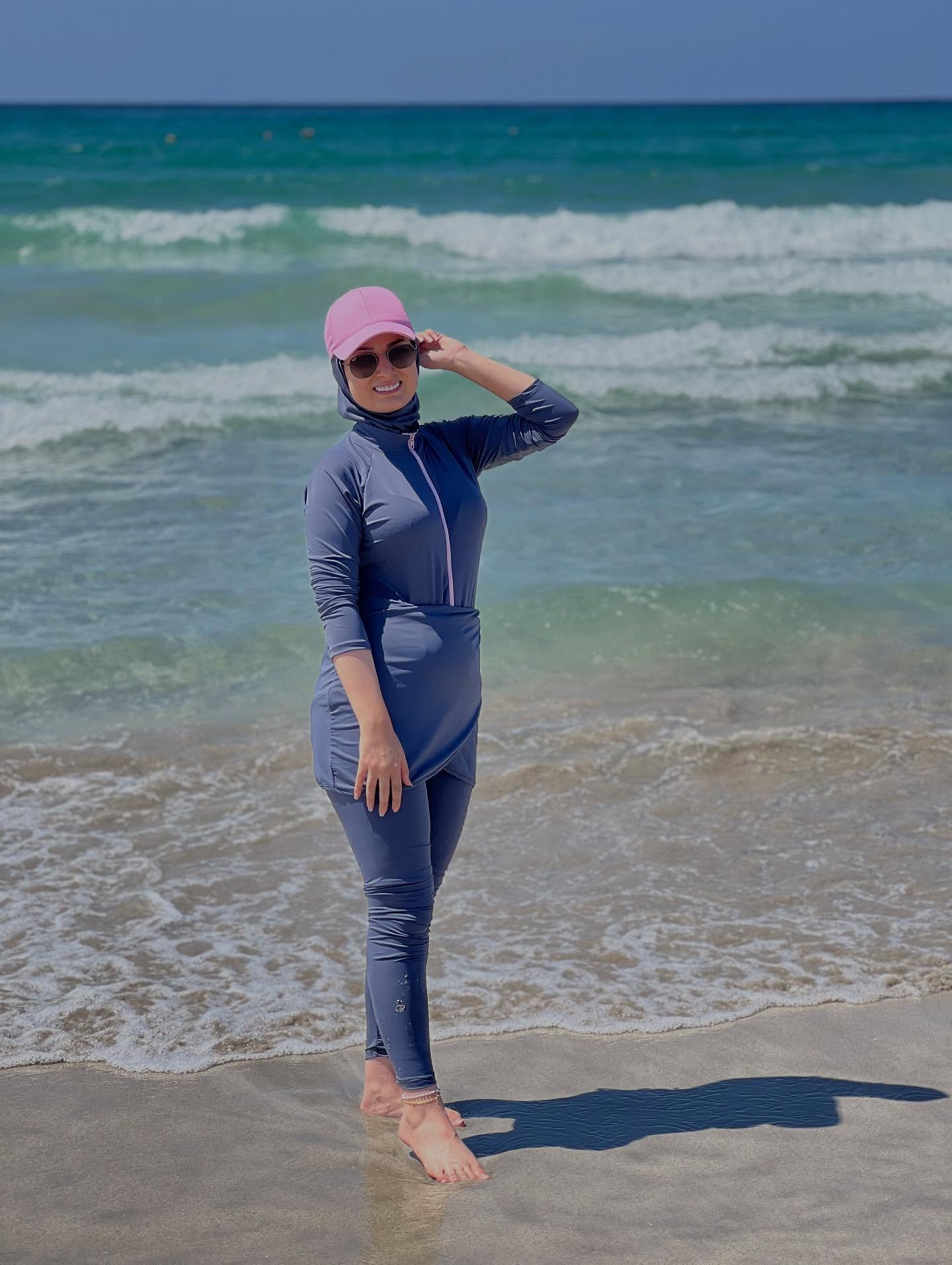 Image of عليا 🇱🇧 from Instagram blue swimsuit, pink cap, sunglasses, beach, barefoot