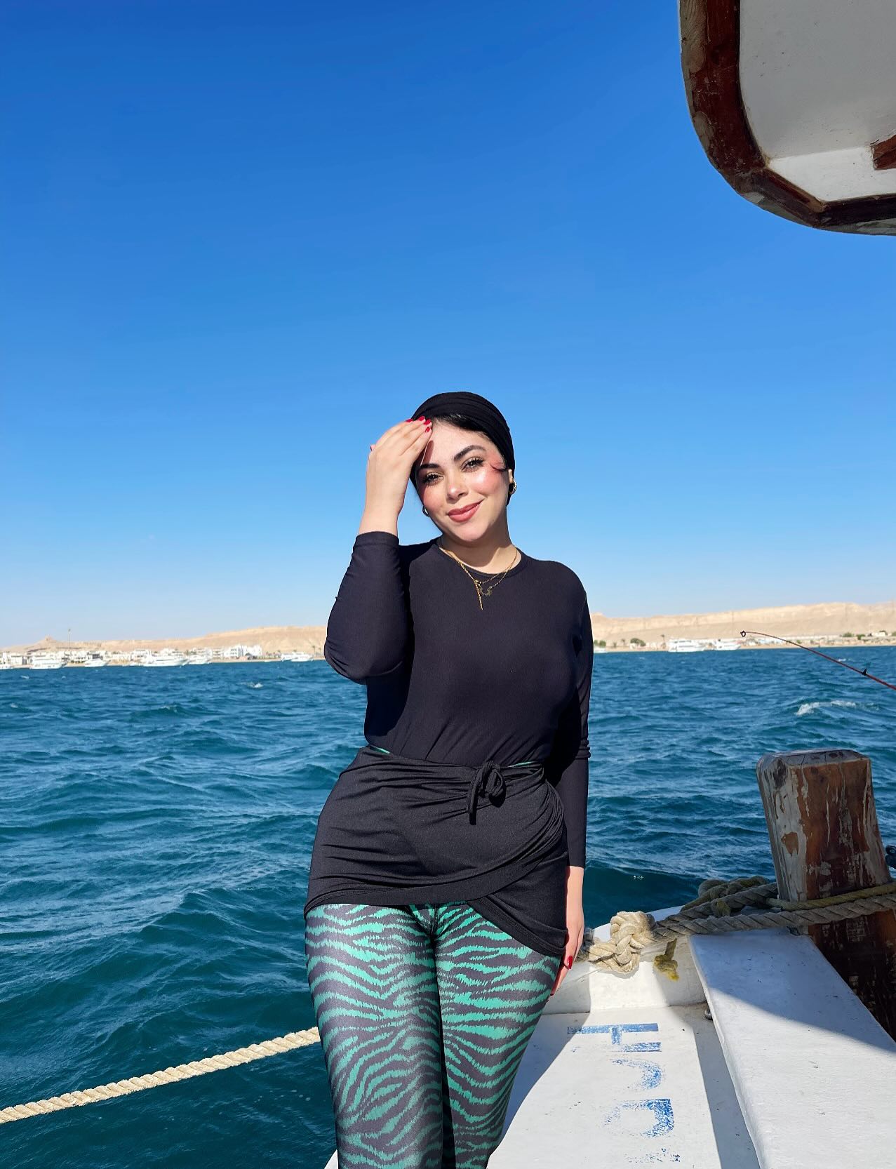 Image of Fatma E Khalifa from Instagram black top, leggings, animal print, headscarf, boat, nautical, water, outdoor