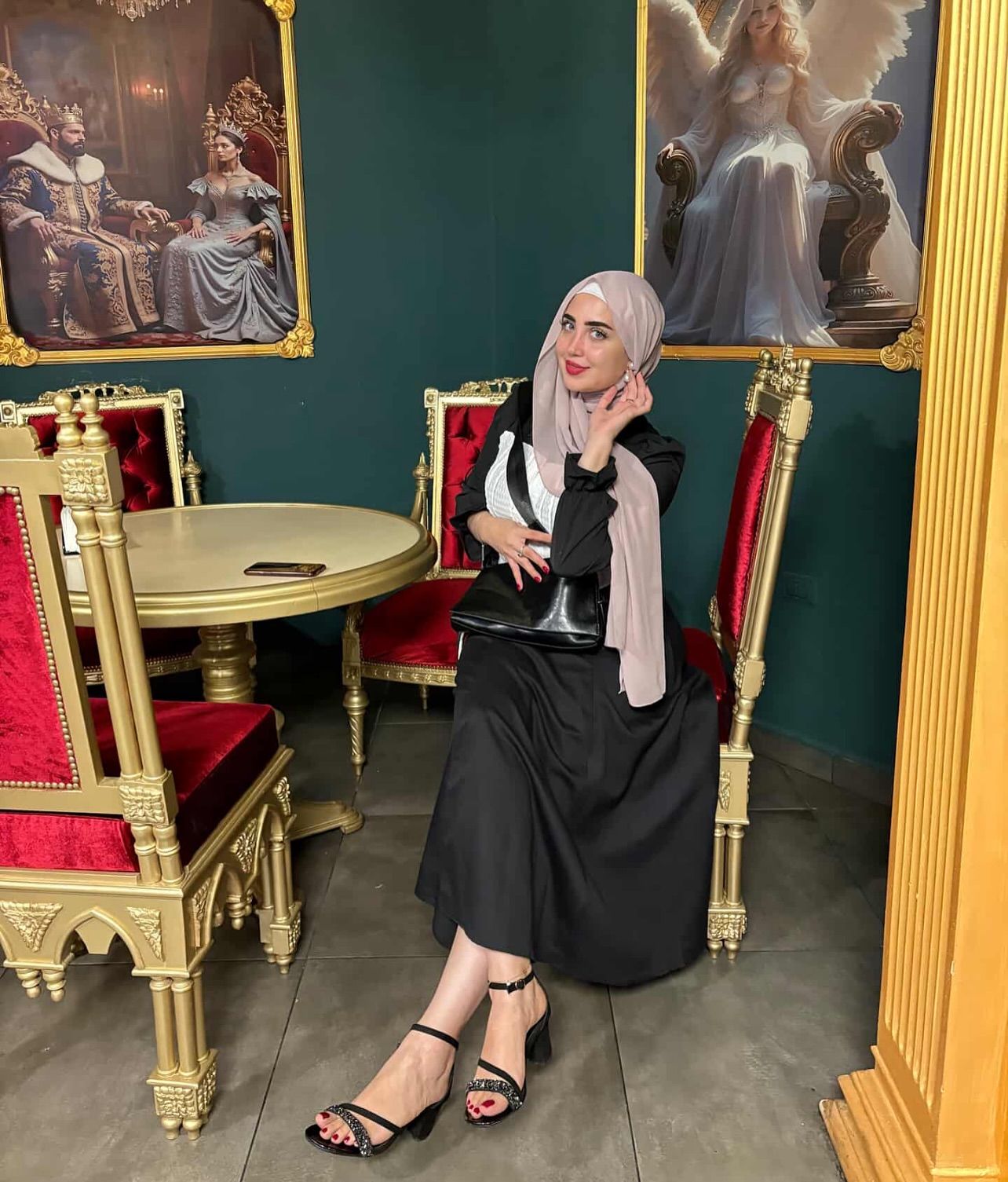 Image of World Models 🩵 from Instagram black dress, hijab, black handbag, strappy heels, ornate decor, red velvet chairs, elegant setting