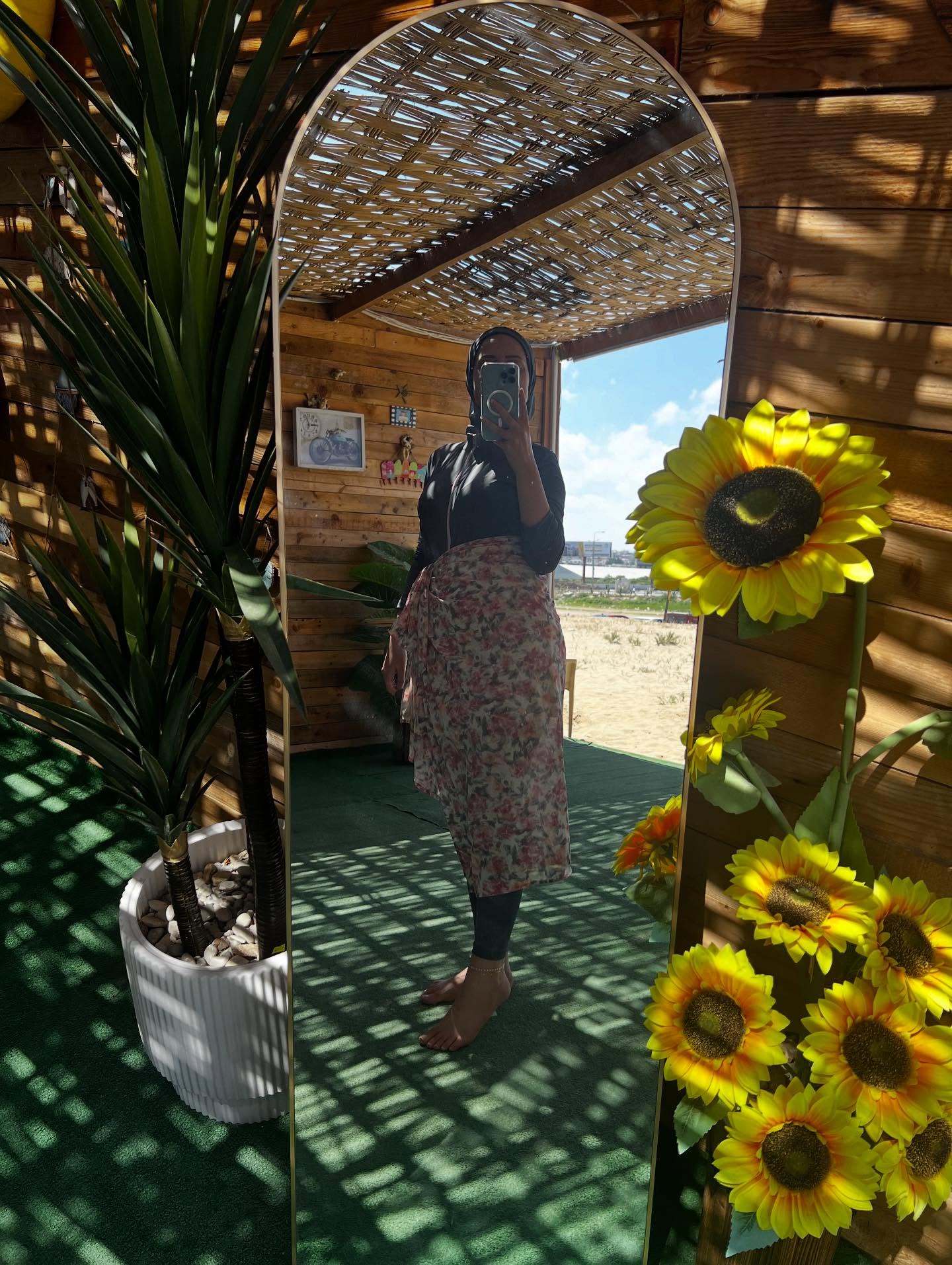 Image of عليا 🇱🇧 from Instagram floral dress, leggings, barefoot, black top, headscarf, outdoor, mirror, sunflowers