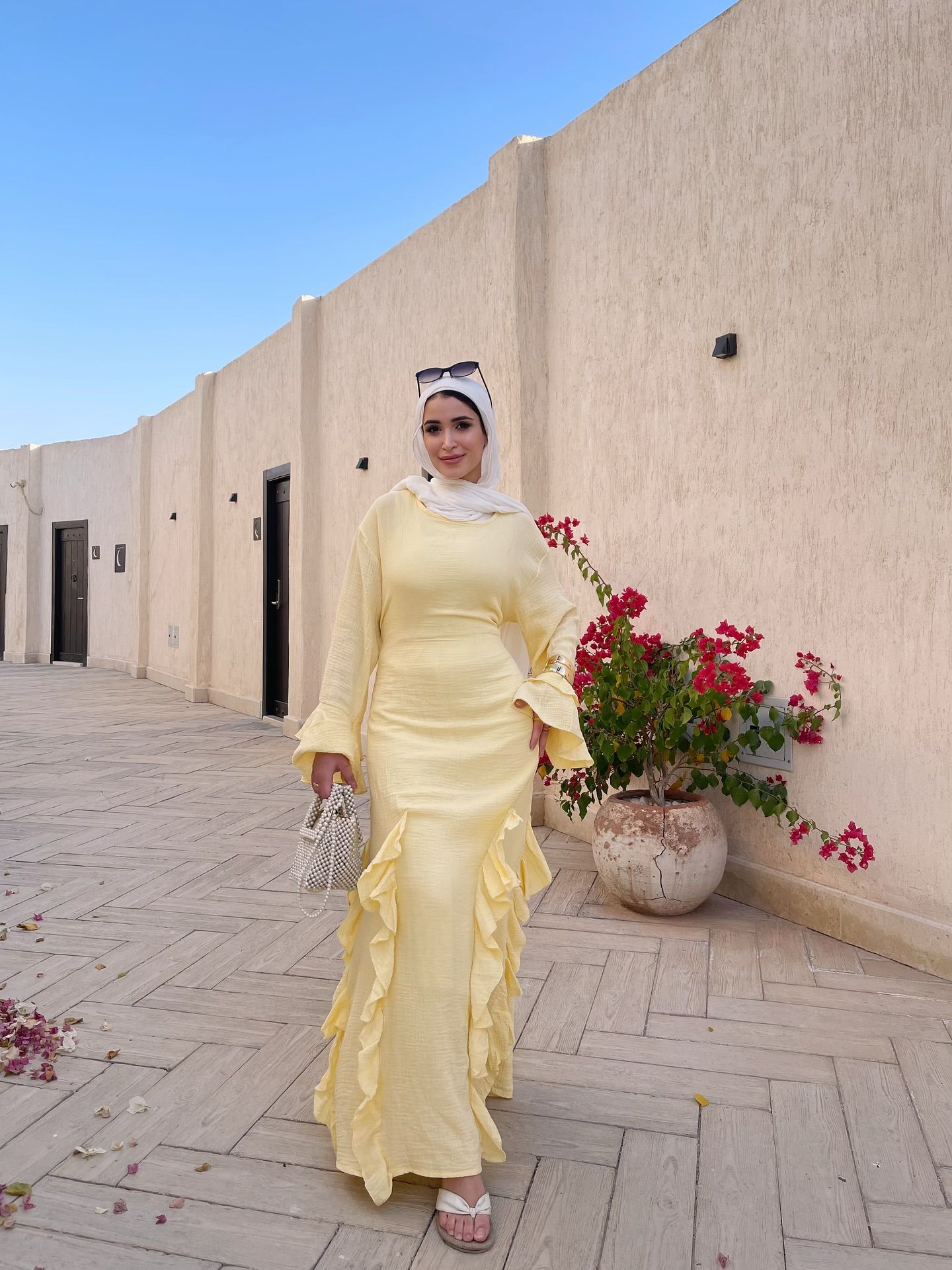 Image of 🅝🅐🅓🅐 🅖🅐🅜🅐🅛 🅨🅐🅗🅘🅐 from Instagram yellow dress, ruffled dress, white hijab, sunglasses, beaded bag, sandals, flower pot, blue sky