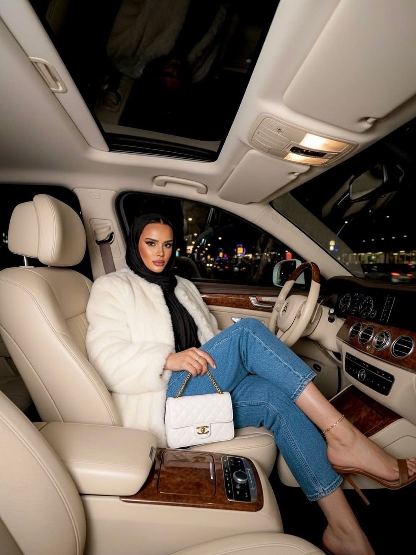 Image of madame.winc from Instagram faux fur coat, denim jeans, white purse, high heels, interior of car, nighttime