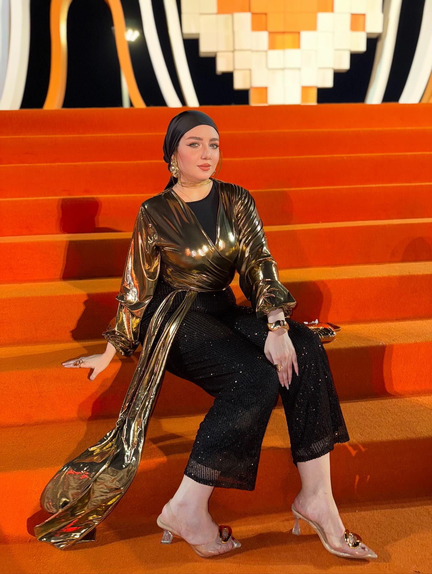 Image of makeup by merna t3ima from Instagram metallic top, black sequin pants, headscarf, clear heels, earrings, bracelet, ring, orange stairs, gold and black
