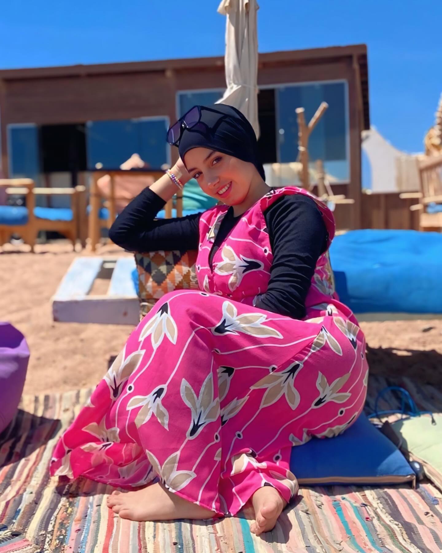 Image of NaDa NabiL-ندي نبيل from Instagram pink floral dress, black long sleeves, black headscarf, sunglasses, beach setting, barefoot