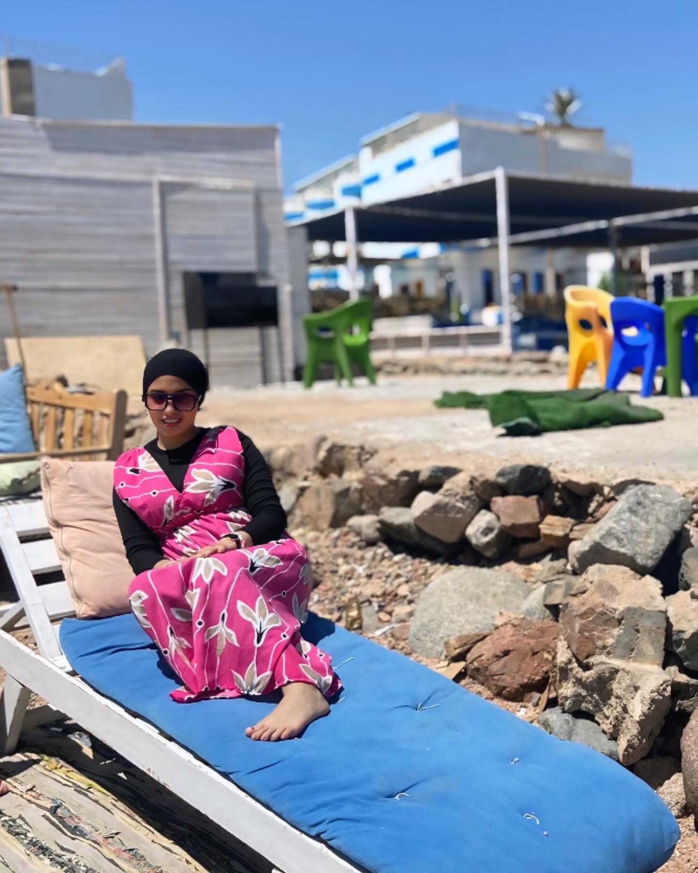 Image of NaDa NabiL-ندي نبيل from Instagram pink floral dress, black top, hijab, sunglasses, barefoot, beachside