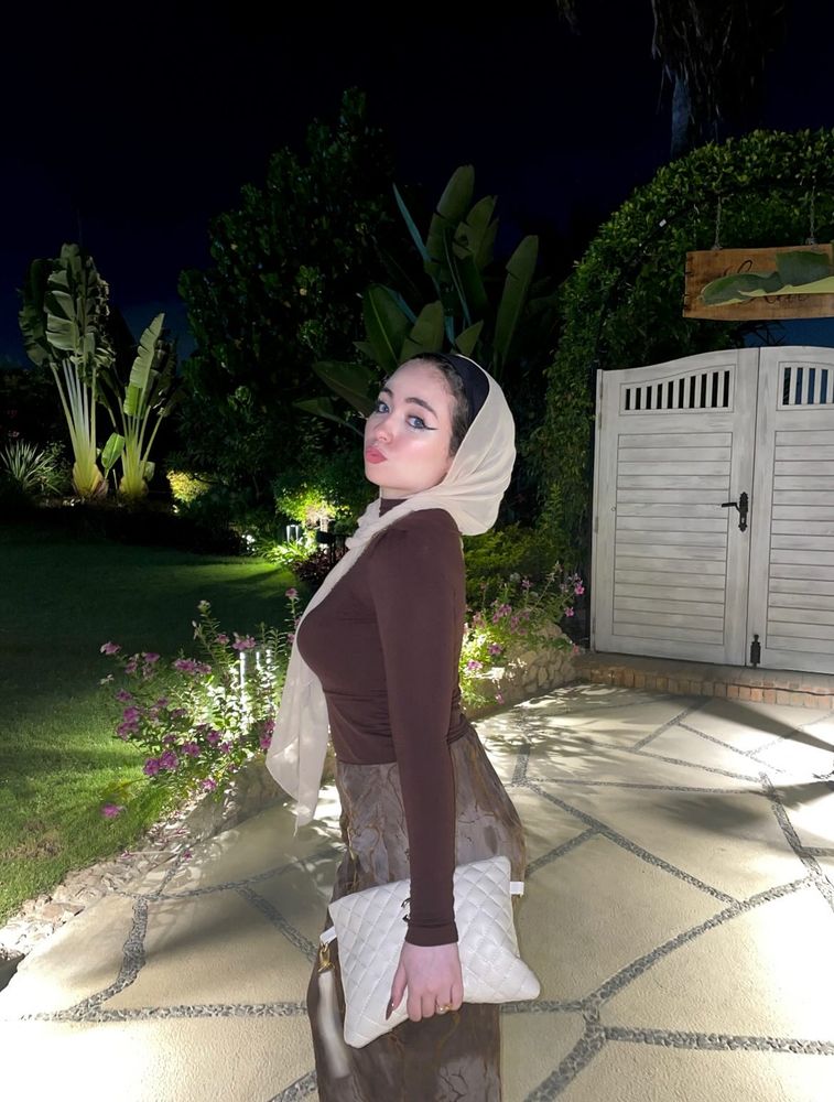 Girl in brown fitted top and light-colored skirt with hijab in a garden setting