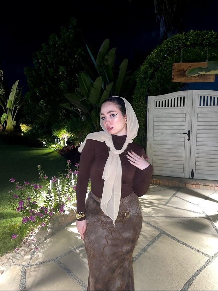 Ashrkat wearing a brown top and patterned skirt with a hijab in a garden setting.