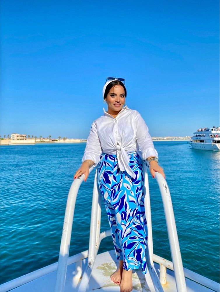 Girl in white top and blue patterned trousers barefoot on a boat.