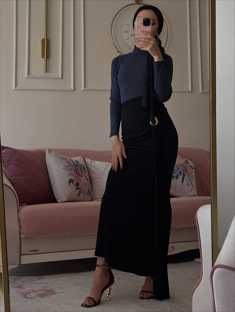 Woman in navy top and black draped skirt with strappy sandals in a stylish setting.