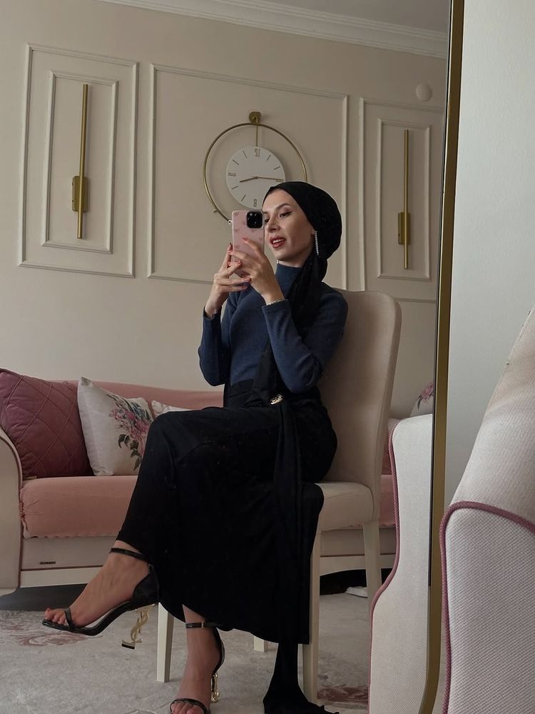 Woman in fitted navy blue top and flowing black skirt with strappy heels in a stylish interior.