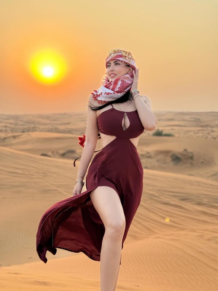 Woman in burgundy dress and headscarf in desert at sunset.