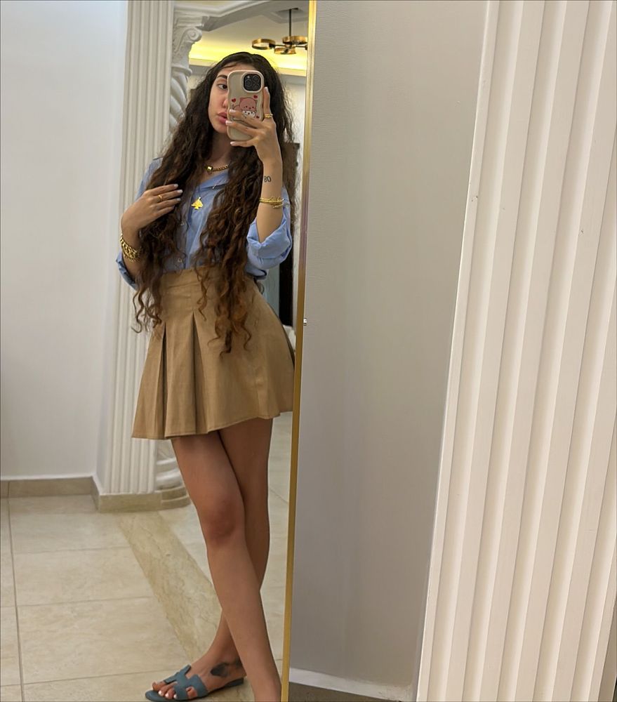 Girl in light blue shirt and beige skirt with blue slide sandals in elegant interior