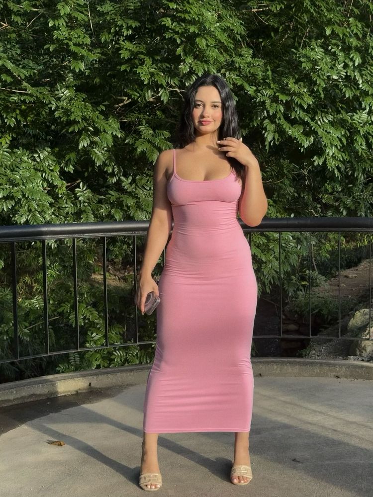 Bárbara in a pink midi dress and strappy heels in a lush green setting.