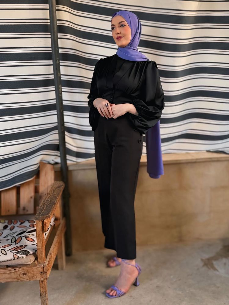 Woman in black top and trousers with lavender strappy heels and purple hijab.