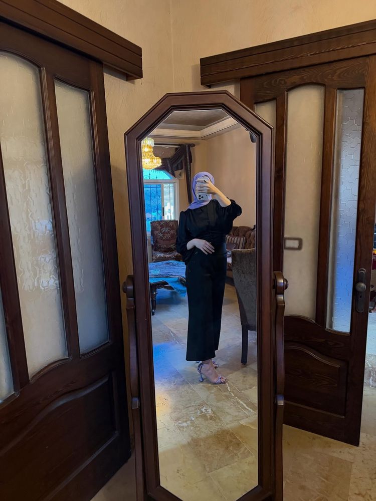 Girl in black top and bottom with silver sandals in front of a mirror.