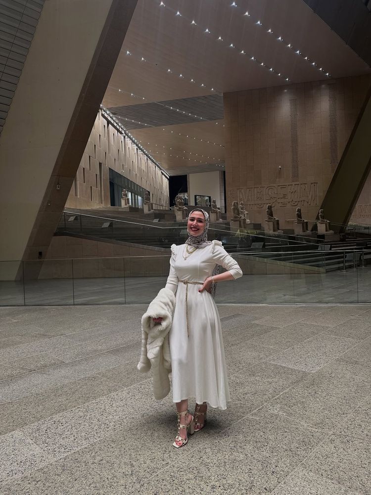 Woman in white dress and strappy heels inside a museum.
