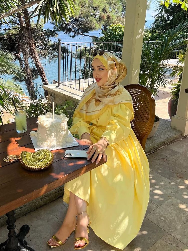 Woman in a yellow dress and golden sandals at an outdoor celebration by the water.