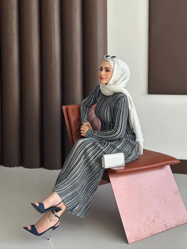 Woman in striped maxi dress and navy stilettos seated elegantly.