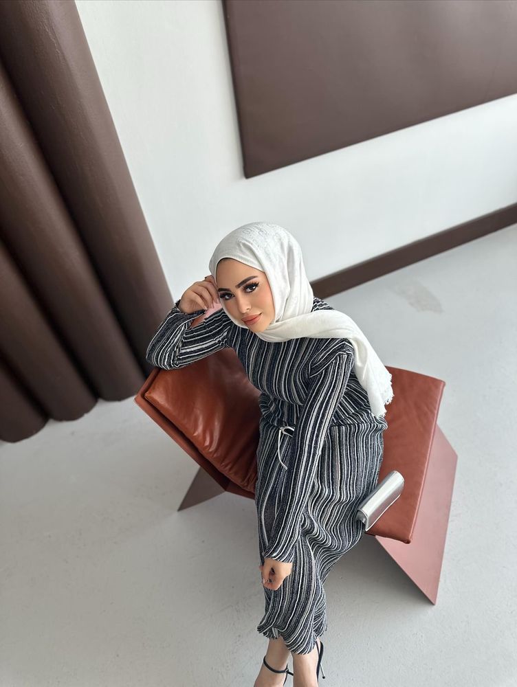 Woman in striped dress and black strappy sandals sitting on a modern chair.