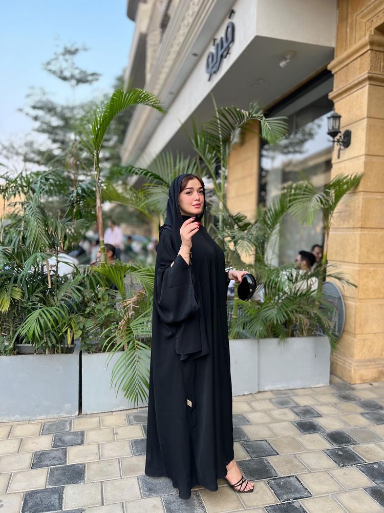 Woman in black abaya and black sandals standing outside.