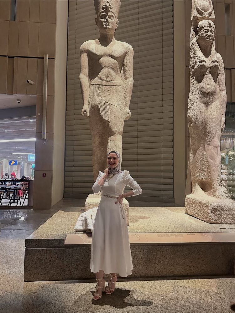 Woman in white maxi dress and strappy heels in front of ancient statues.