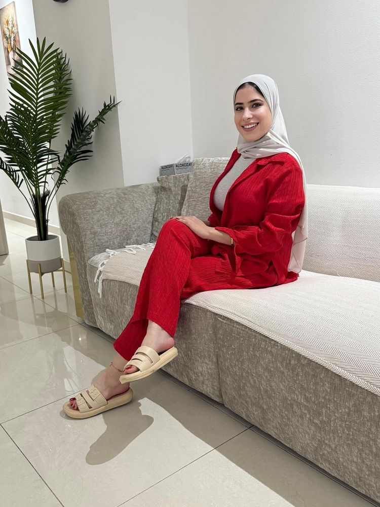 Woman in chic red outfit and cream slides sitting on a sofa indoors.