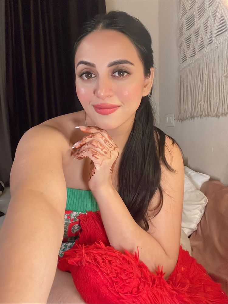 Woman in a floral green top with henna on her hand in a cozy setting