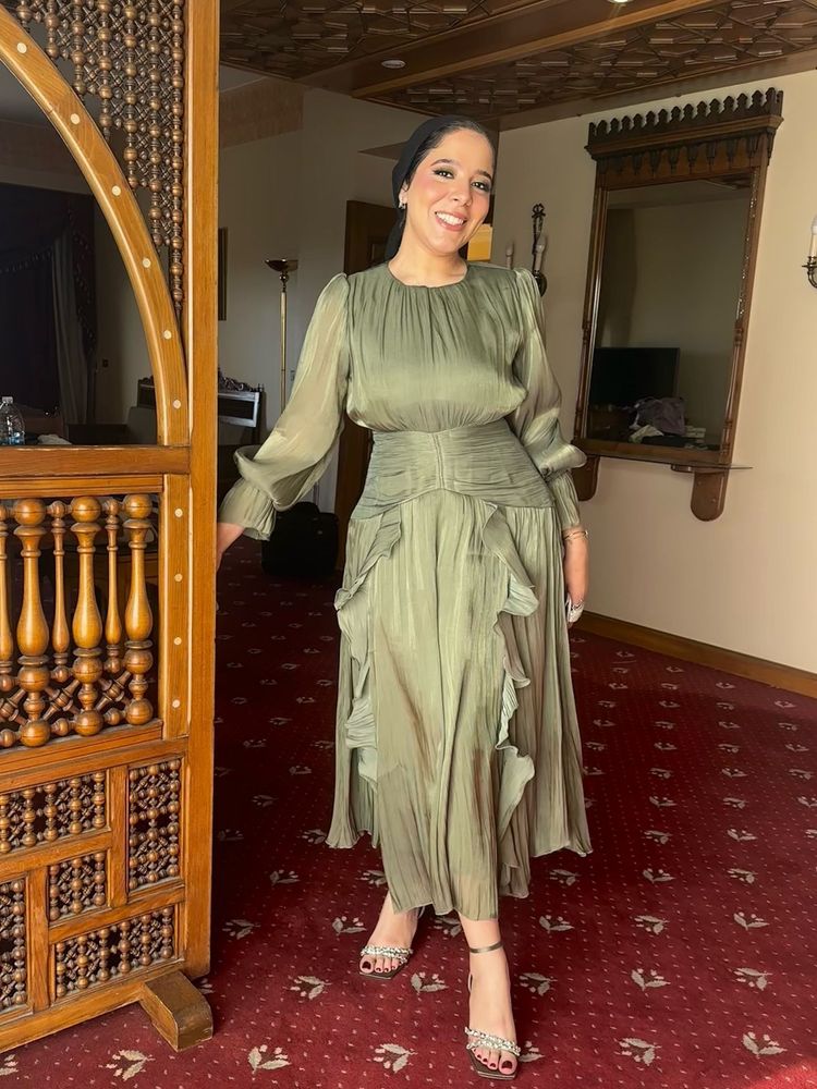 Woman in olive green layered dress and strappy heels in an elegant setting.