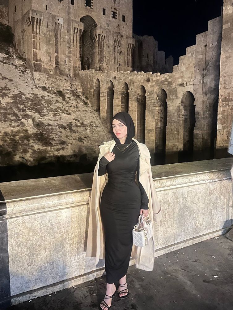 Woman in a black dress and strappy sandals against a historic stone backdrop.