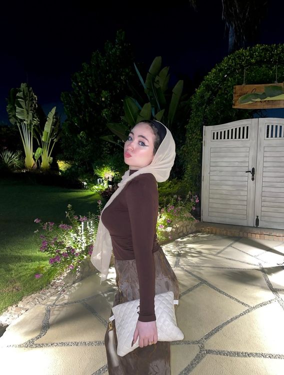 Girl in brown fitted top and light-colored skirt with hijab in a garden setting
