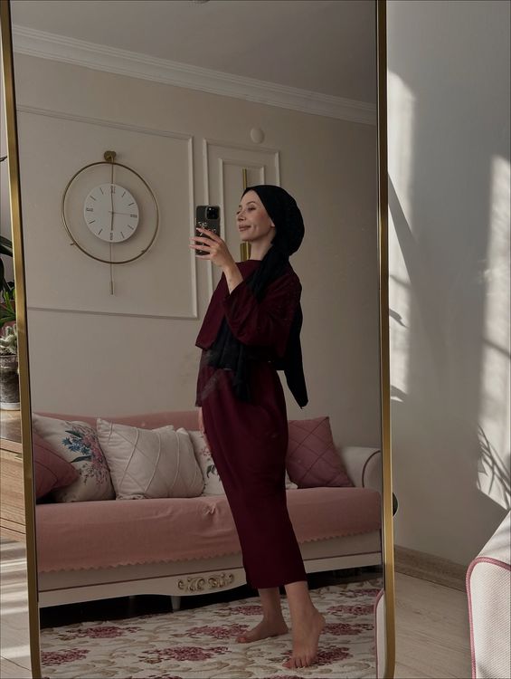 Woman in maroon loungewear and hijab in a cozy living room.