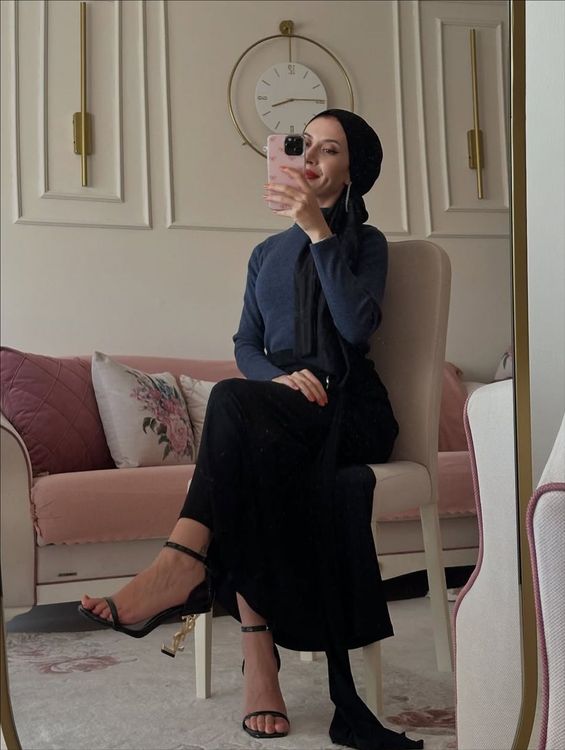 Woman in navy long-sleeved top, black skirt, and strappy heels in a stylish room.