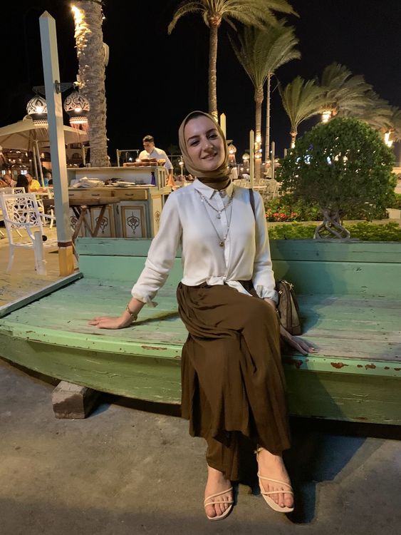 Girl in white blouse and brown maxi skirt wearing strappy sandals in a vibrant outdoor setting.