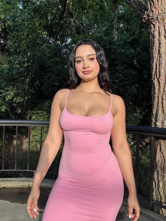 Woman in a fitted pink dress standing in a green park setting.