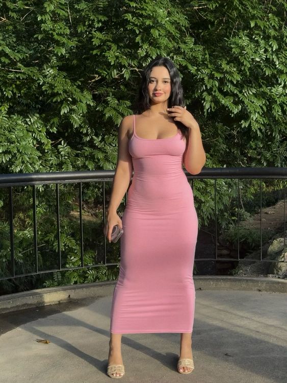 Bárbara in a pink midi dress and strappy heels in a lush green setting.