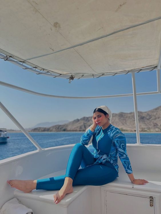 Woman in blue swimwear and hijab relaxing on a boat.