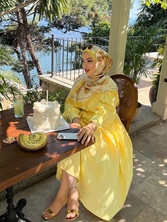 Woman in a yellow dress and golden sandals at an outdoor celebration by the water.