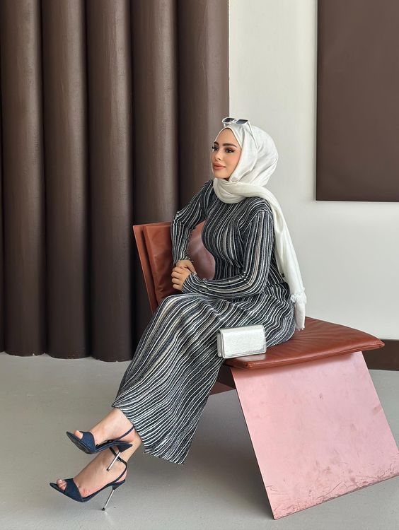 Woman in striped maxi dress and navy stilettos seated elegantly.