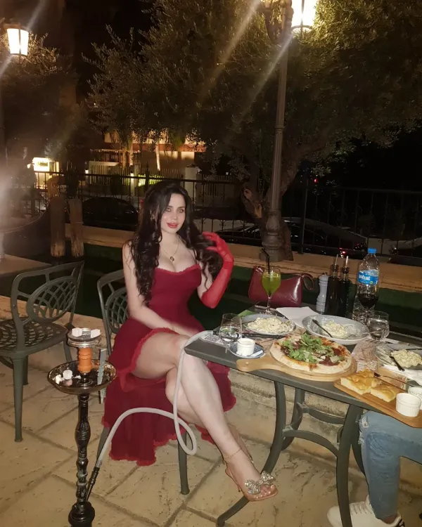 Woman in elegant red dress and strappy heels at an outdoor dining setting.