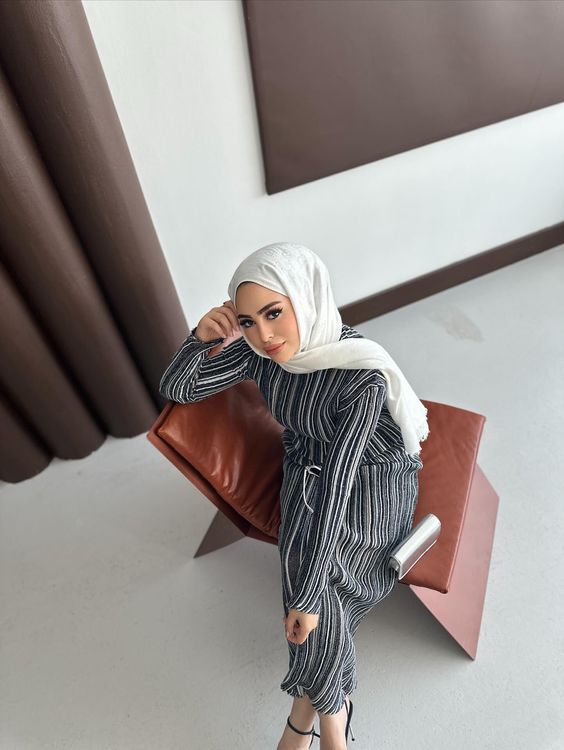 Woman in striped dress and black strappy sandals sitting on a modern chair.