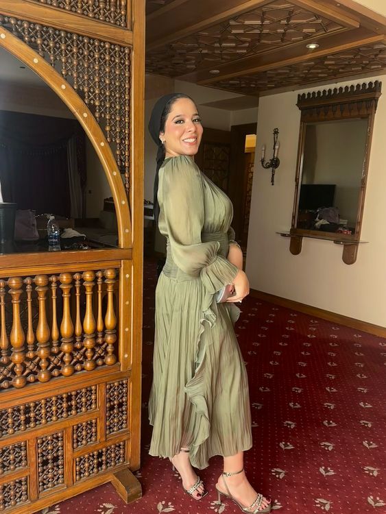 Woman in olive green dress and transparent sandals in an ornate interior.