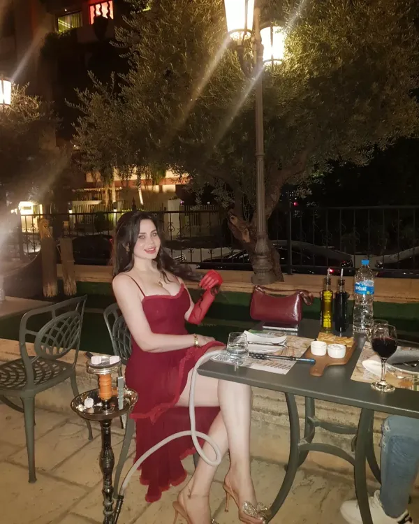 Woman in a red dress and strappy heels seated at an outdoor table.