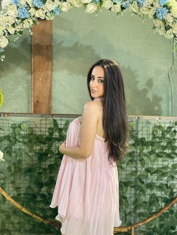 Girl in a flowy pink dress standing against a floral backdrop.
