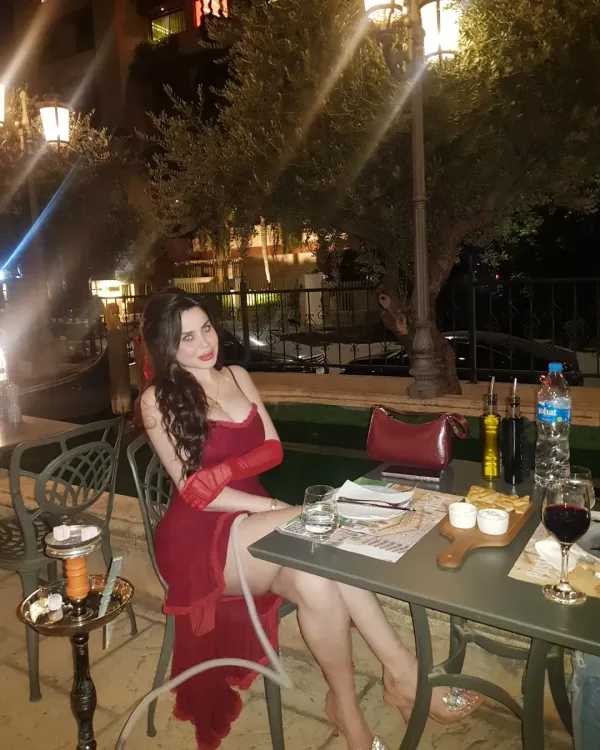 Woman in a red off-shoulder dress sitting at an outdoor dining table.